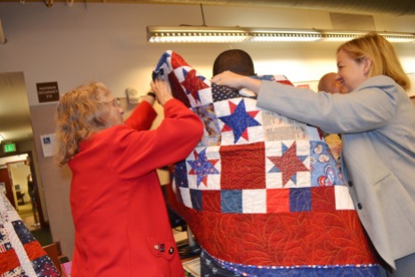 Jarenie Trachier & Judge Linda Bell wrap a veterans' court graduate with a quilt specially made by the Quilts of Valor non-profit organization.